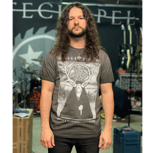 Load image into Gallery viewer, image of a man with curly long hair wearing an oil washed black t standing in the whitechapel music studio. tee has full body print in white of a deer wearing a cloak outside in the woods. at the top says whitechapel and the bottom says there&#39;s nowhere left to run

