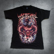 Load image into Gallery viewer, Image of a black tshirt against a concrete background. Across the chest of the shirt in orange to yellow/white gradient text reads &quot;whitechapel&quot;. Below that is an image of an angry animal skull with tusks or horns coming out of its head. This is in orange. In its mouth it is holding an orange and yellow sawblade with three black stars in the center of the sawblade.
