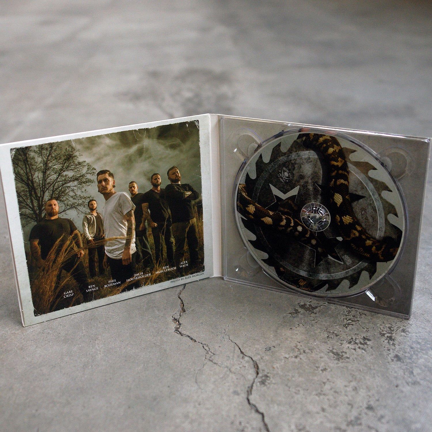 image of the inside of an opened gatefold CD on a concrete floor. The inside left is a photo of the six male members of the band, Whitechapel standing outside in front of a tree, the right shows the CD with a sawblade and snake on the CD