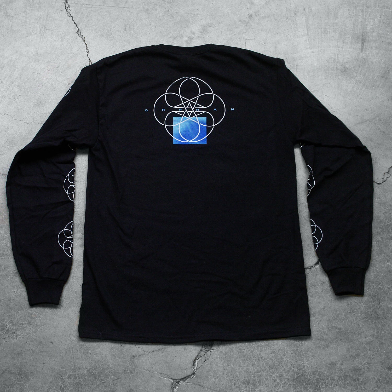  Image of the back of a black long sleeve against a grey concrete background. The sleeves feature a white circle abstract design with lines and two stars in the center making a double pentagram. The back center of the shirt near the shoulders features a white circle outline with abstract lines in the center, and two stars making a double pentagram. a blue square is underneath this. In small blue text reads "orphan". This is placed across the circle design.