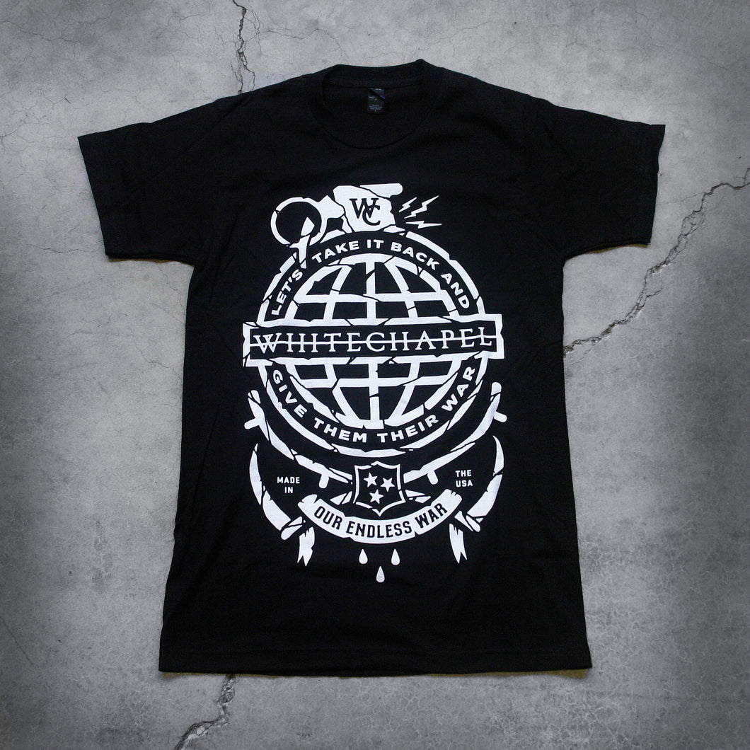 Image of the front of a black tshirt against a grey concrete background. There is a graphic of a white grenade and in there is a globe in the center of it with the text 