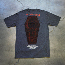 Load image into Gallery viewer, Image of the back of a heather charcoal tshirt against a grey concrete background. the top of the tee near the shoulders reads &quot;the other side&quot;. it is in red text. below this is a graphic of a coffin with a black double pentagram (two stars mirroring and slightly overlapping each other) on the center of it. Below this in white text reads once in the dirt, now above the clouds. i am now free, i am god like.
