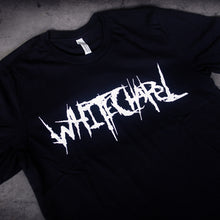 Load image into Gallery viewer, close up, angled image of a black tee shirt laid flat on a concrete floor. tee has center chest print in white that says whitechapel
