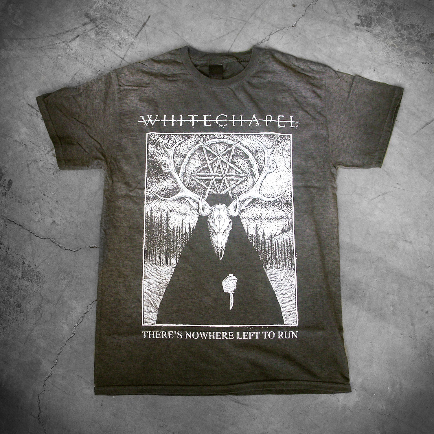 image of a oil washed black tee shirt laid on a concrete floor. tee has full body print in white of a deer wearing a cloak outside in the woods. at the top says whitechapel and the bottom says there's nowhere left to run