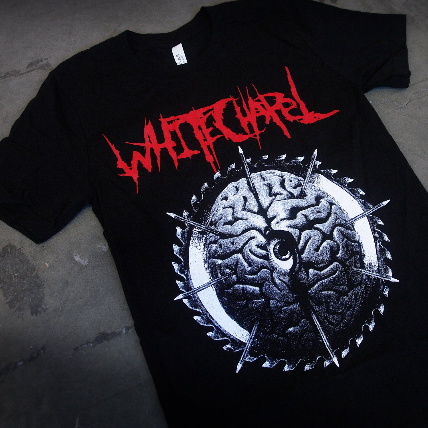 image of a black tee shirt laid flat on a concrete floor. front of tee has full body print of a black and white image of a brain. at the top, in red says whitechapel
