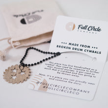 Load image into Gallery viewer, Image of a light colored jewelry bag, paper from full circle company, and black bead chain necklace with a silver metal sawblade with three stars cut out in the center of it against a white background. The paper gives information about how the jewelry is made from a broken drum cymbal rather than be thrown away.
