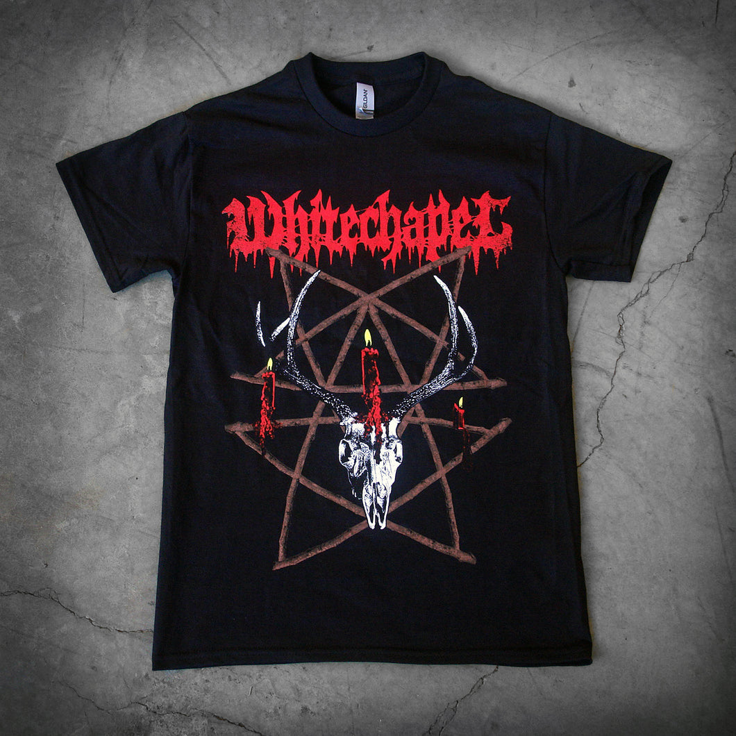 image of a black tee shirt laid flat on a concrete floor. front of tee has full body print. at the top in red says whitechapel. below is a deer skull with a burning candle and a pentagram made out of sticks.