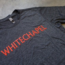 Load image into Gallery viewer, up close Image of the front of a heather charcoal tshirt against a grey concrete background. across the chest in red text reads &quot;whitechapel&quot;.
