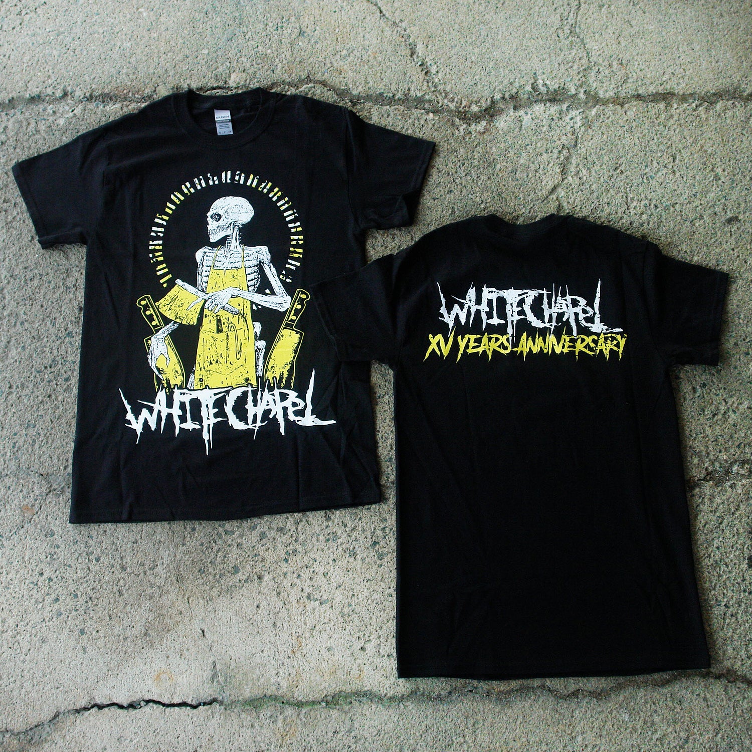 Image of the front and back of a black tshirt against a grey concrete background. The front of the shirt has a yellow skeleton sitting down with its head facing to the left, wearing a yellow apron and holding a yellow knife. Two other knifes are on each side of the skeleton. Below this in white heavy metal style font reads 