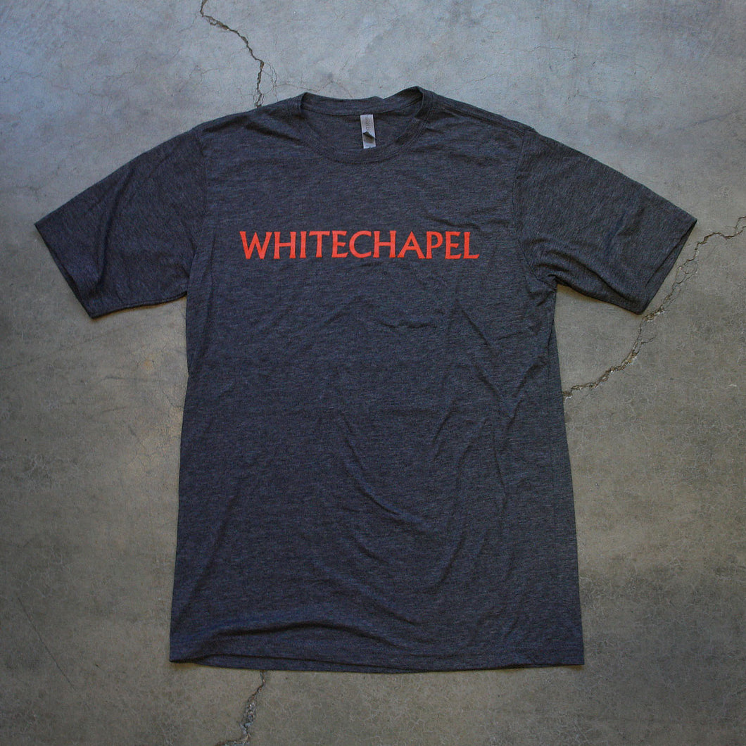 Image of the front of a heather charcoal tshirt against a grey concrete background. across the chest in red text reads 