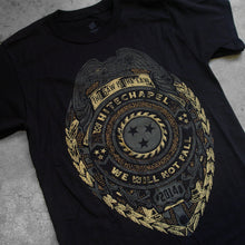 Load image into Gallery viewer, close up, angled Image of a black tshirt against a concrete background. The shirt is a graphic of a badge. There is a bird at the top, and below that it says the saw is the law. the center of the badge has a circle with a sawblade with three stars on the inside of the saw blade. Wrapped around the circle reads &quot;whitechapel, we will not fall&quot;. Below this it says 2014. The graphic is a faded grey/gold and black color.
