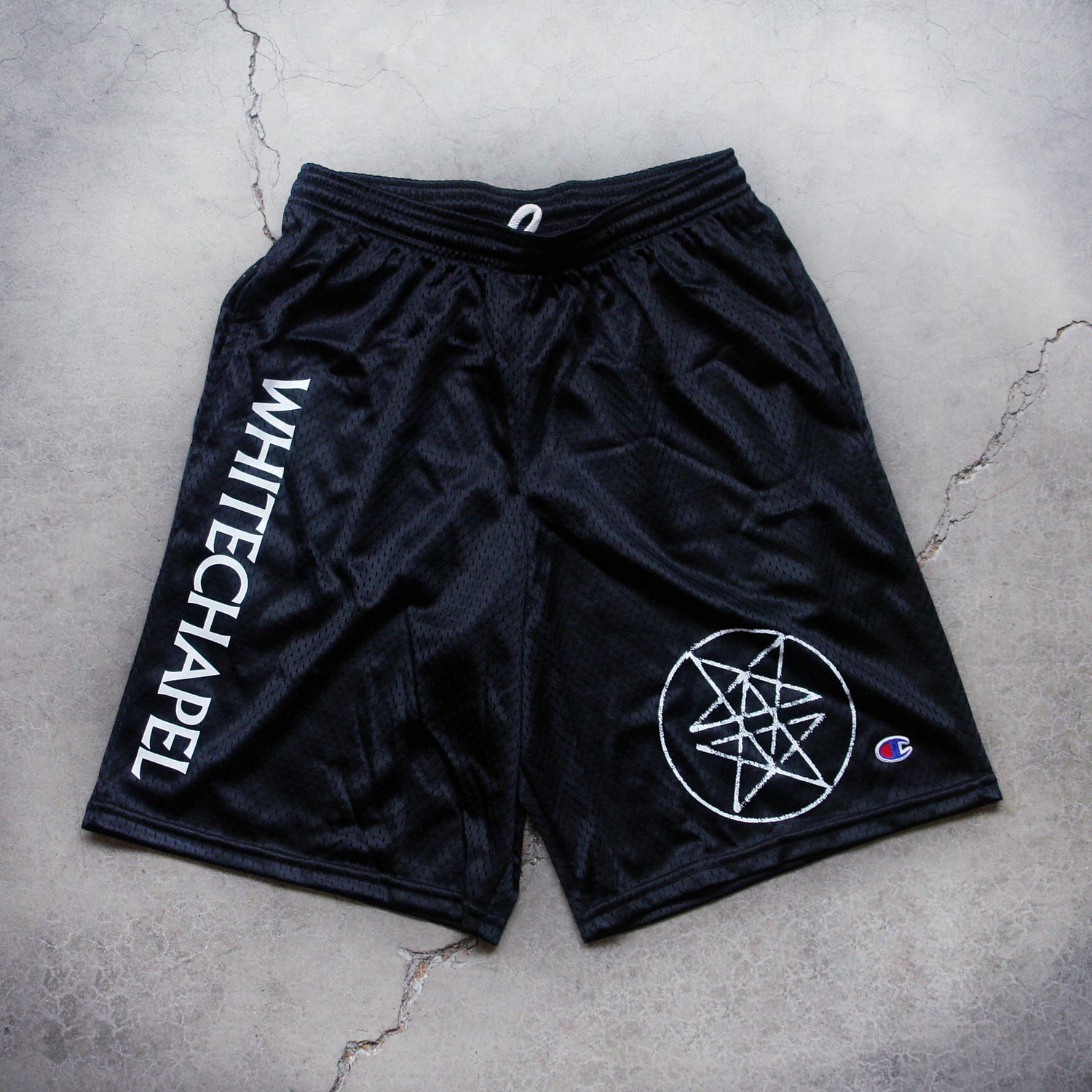Image of black shorts against a grey concrete background. The shorts are athletic style with a drawstring. Descending down the right leg in white text says 