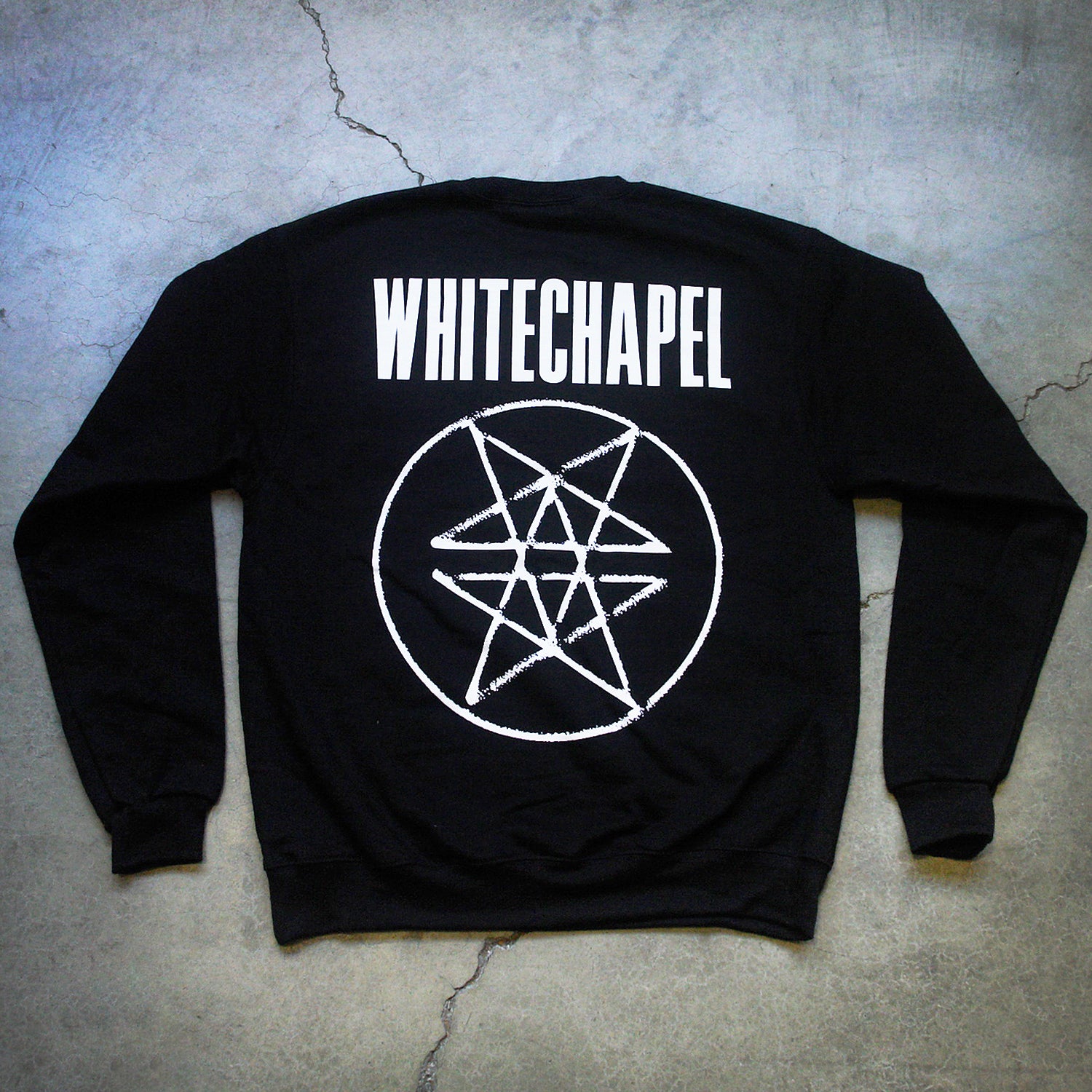 Image of the back of a black crewneck against a grey concrete background. Across the shoulder area of the crewneck in big white letters says "whitechapel". Below that is what is called a double pentagram, it is a white circle with two stars mirroring and slightly overlapping each other on the inside of the circle.