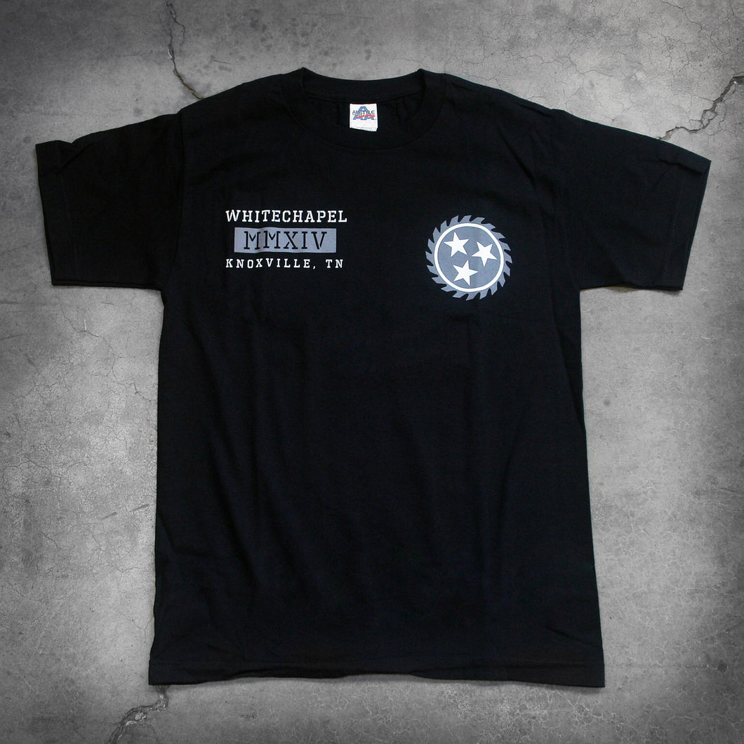 image of the front of a black tee shirt on a concrete background. the front of the tshirt has a grey sawblade with three white stars in the center of the sawblade on the left chest. The right chest says whitechapel, mmxiv, knoxville tn in a grey white text.