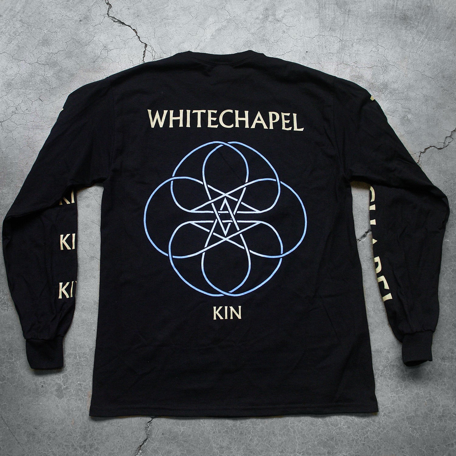 Image of the back of a black longsleeve against a grey concrete background. The left sleeve says "Kin" on it 5 times in white text. the right says "whitechapel", just once, in white text. The back of the longsleeve reads "whitechapel" across the shoulders in white text. Below this is an abstract thin lined pattern in white and blue. It loosk like a circle with lines and stars in the center. Below this in white text reads "kin".