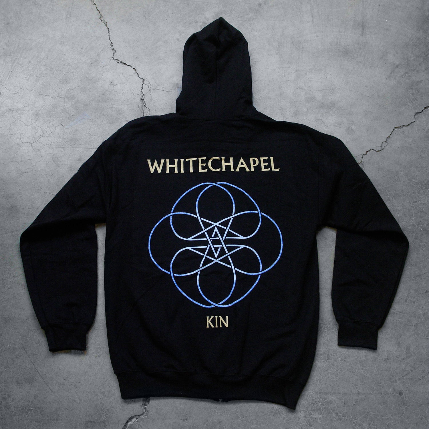 Image of the back of a black zip up sweatshirt against a grey concrete background. Across the shoulder area in white text reads "whitechapel". Below this is a circular lined abstract design with two stars in the center, designed to look like a double pentagram. This is white and blue. Below this design in white text reads "Kin".