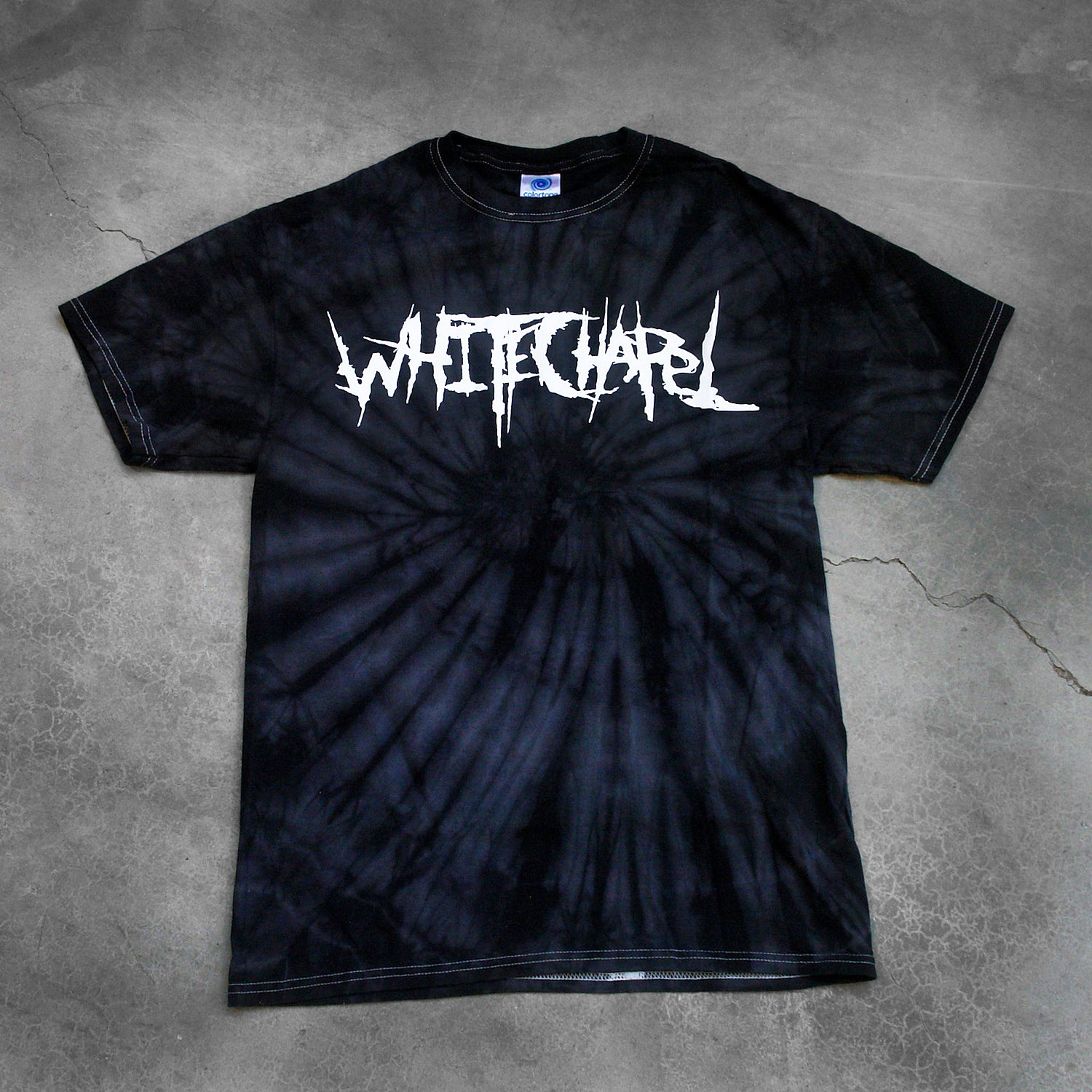image of a black spider tie dye tee shirt on a cracked concrete background. tee has front center chest print across in white that says Whitechapel