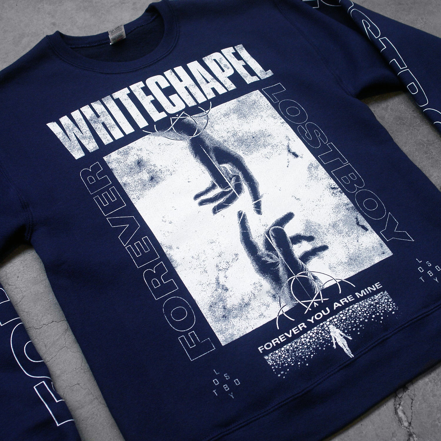 close up  Image of a black crewneck against a grey concrete background. Across the chest in white distressed text reads "whitechapel". below this is a white square with two hands reaching to touch each other from the top and bottom of the swuare. The sides of the swuare in white outline text reads forever lost boy. the bottom of the square in white text says forever you are mine with a white silhouette. the left sleeve says lost boy and the right sleeve says forever, both in an outlined white text.