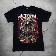 Load image into Gallery viewer, Image of the front of a black tshirt against a grey concrete background. the shirt features a red, white, black, and bluish gray graphic of a an animal skull with a third eye holding a scythe and wearing a cloak. Its ribs are showing. There are skull heads all around the monster. There is a red background behind the graphic.
