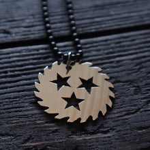 Load image into Gallery viewer, Image of a silver colored sawblade necklace against a black wooden background. The chain is made of black beads and has a silver metal sawblade with three stars cut out in the center of it on it. 
