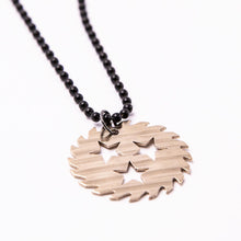 Load image into Gallery viewer, Image of a silver colored sawblade necklace against a white background. The chain is made of black beads and has a silver metal sawblade with three stars cut out in the center of it on it.
